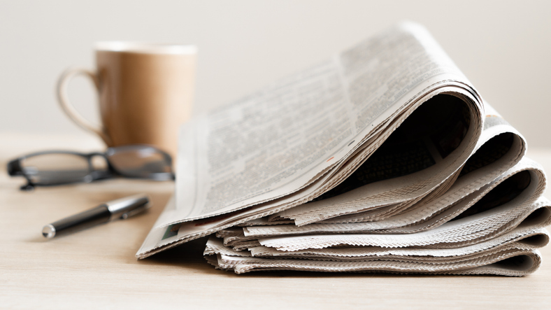 Newspapers on a table with pens and a coffee mug