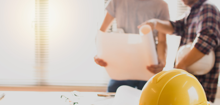 Two workers reviewing a plan with a yellow hat in the foreground