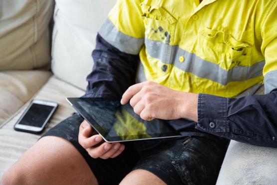 Worker in high visibility work gear scrolling through an iPad